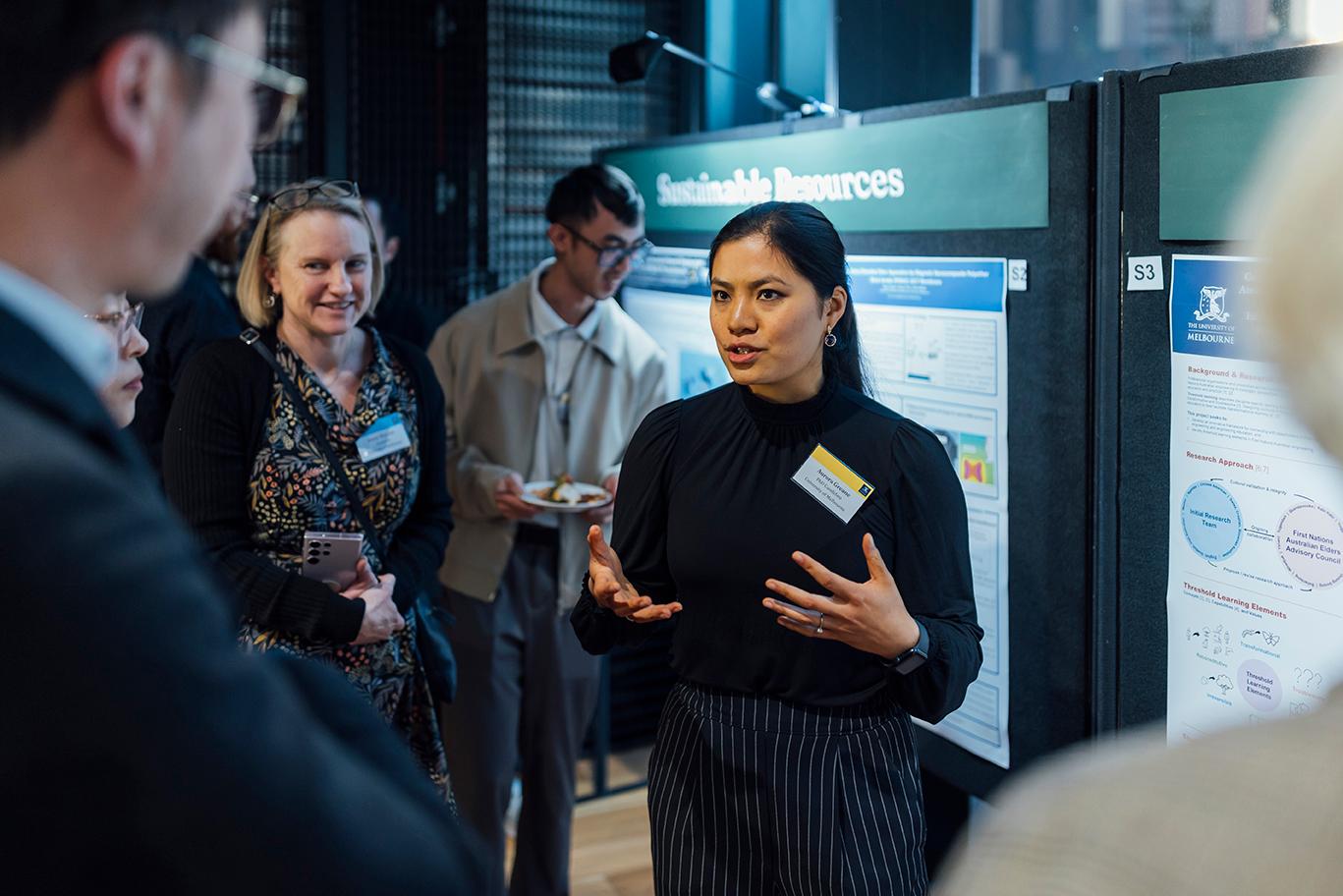 A graduate researcher presents a Sustainable Resources research project in front of a poster board.